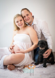 Babybauchfoto Familie sitzt am Boden mit ihrem Hund. Familienfotografie im Raum Linz-Amstetten.